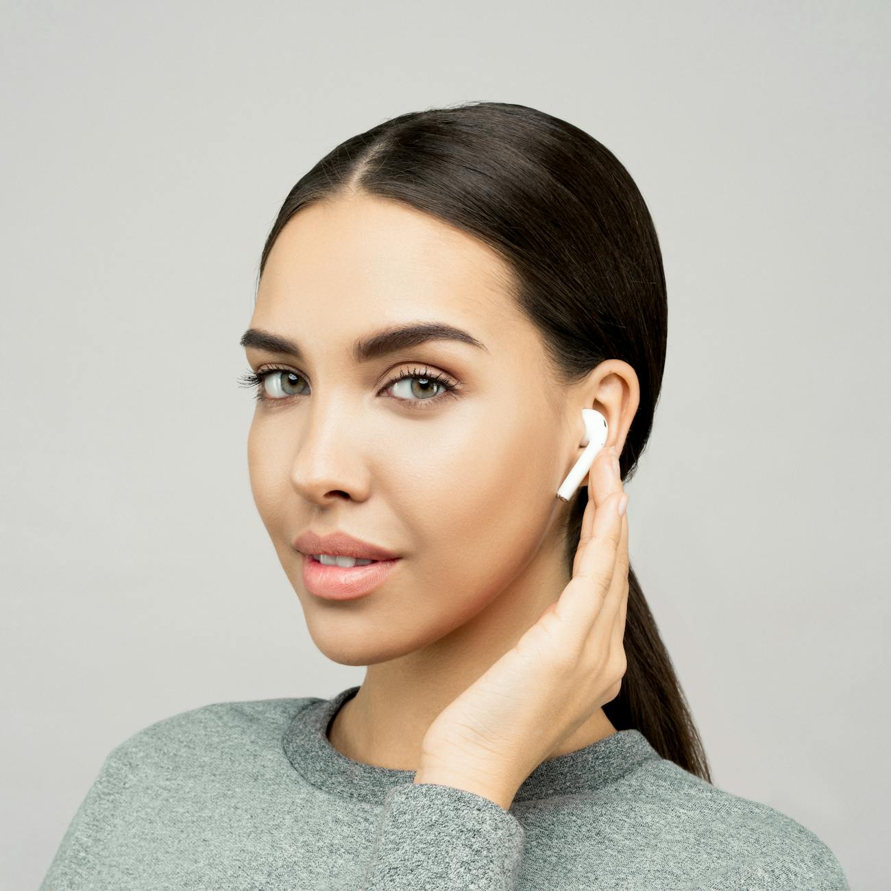 Close-up portrait of a smiling woman wearing wireless earbuds indoors.